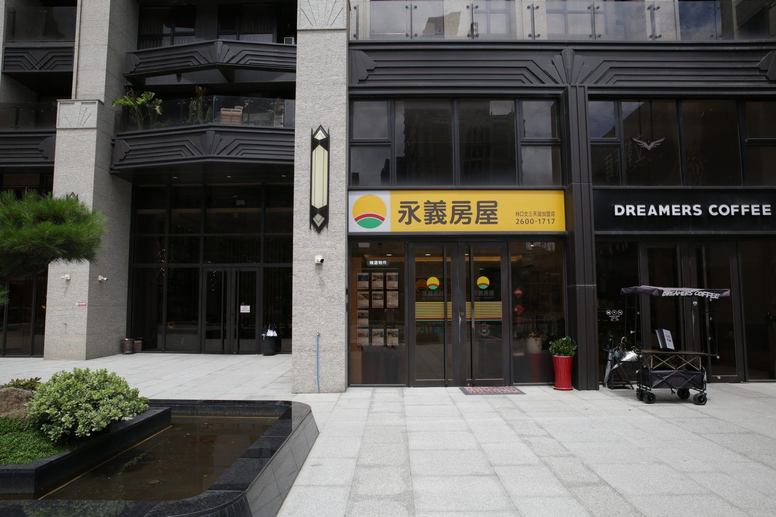 大樓一樓入口，右邊是 DREAMERS COFFEE 的黑色招牌，左邊是永義房屋的黃色招牌