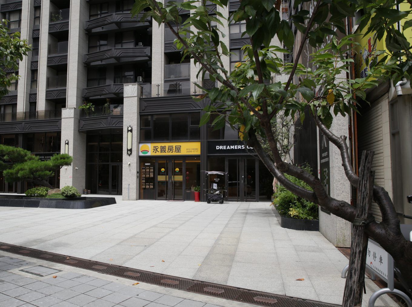 從中庭方向看入口，前方有松樹和水景，後面是大樓的玻璃門